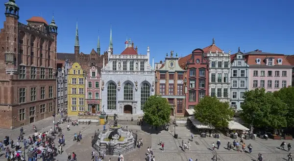 Tętniący życiem gdański plac z Dworem Artusa, fontanną Neptuna i kolorowymi kamieniczkami.