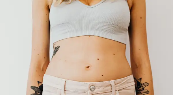 En kvinna med tatueringar på armarna och magen, som visar sin mage som kan vara känslig för gluten.
