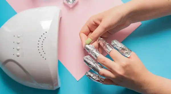 Rimozione smalto semipermanente: unghie avvolte in stagnola, lampada UV e glitter. Attenzione, il semipermanente rovina le unghie se non rimosso correttamente.