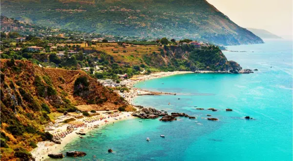 Vista mozzafiato del capo Vaticano a Tropea, con il mare cristallino che lambisce le spiagge affollate e le scogliere verdi.