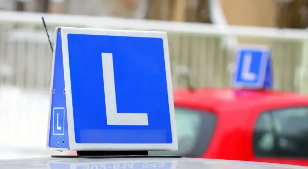 Tablica z literą "L" na dachu samochodu, symbolizująca naukę jazdy. Chcesz wiedzieć, jak zapisać się na prawo jazdy?
