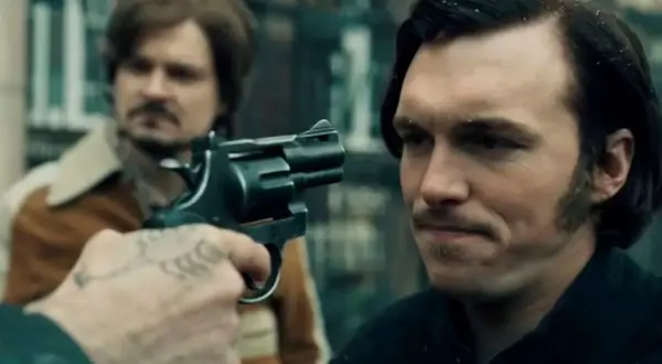 Scena z filmu, gdzie gangster celuje z rewolweru. Może to być moment z "Jak pokochałam gangstera", pełen napięcia i niepewności.