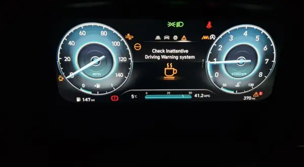 Panel de Hyundai i20 con fallo: "Check Inattentive Driving Warning system" y taza de café.