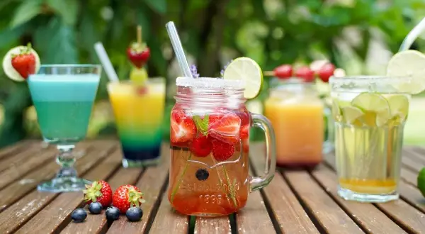 Mehrere bunte, fruchtige alkoholfreie Cocktails mit Beeren und Limette auf Holztisch.