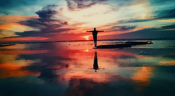 Zachód słońca na plaży, człowiek z rozłożonymi ramionami. To jak praca z przekonaniami, ćwiczenia na wolność i akceptację.