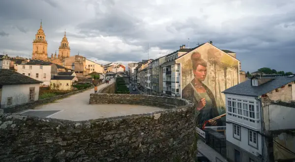 Mural de una mujer en la muralla de la fortaleza Lugo, con la catedral al fondo y un cielo nublado.