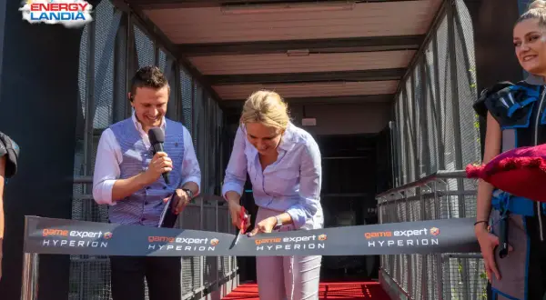 Kobieta przecina wstęgę z napisem "game expert HYPERION", mężczyzna trzyma mikrofon.