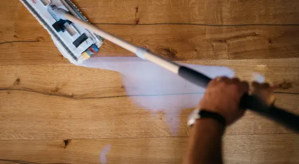 Mano che pulisce un pavimento in legno non trattato con uno straccio umido.