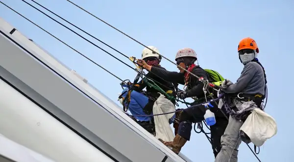 Trzech alpinistów pracujących na wysokości, każdy w kasku i uprzęży. Za stan bezpieczeństwa i higieny pracy w zakładzie odpowiada ich profesjonalizm.