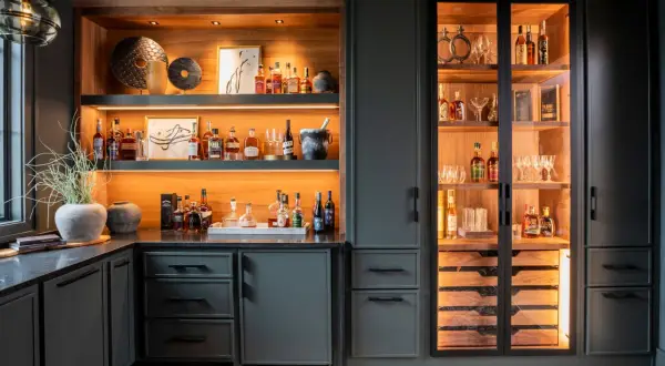 Stylish basement bar ideas featuring illuminated shelves stocked with liquor bottles, glassware, and decorative items.