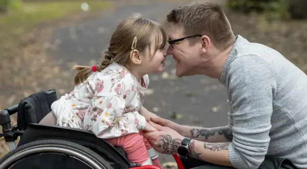 Padre e figlia si toccano il naso, lei in carrozzina. Un momento di gioia che celebra i diritti genitori con figlio disabile.