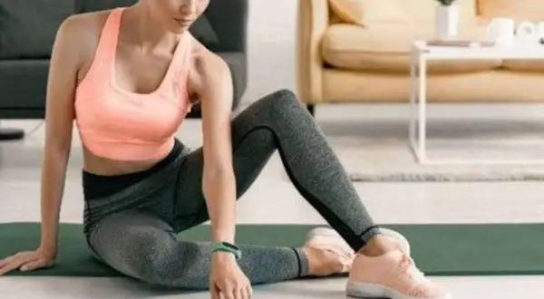 Frau in Sportkleidung sitzt auf einer Matte und bedient ihr Smartphone.