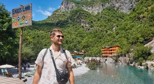Ein Mann genießt die atemberaubende Landschaft Albaniens. Ein Schild weist auf "Eagles Land Guest House" hin, ein perfektes Ziel für Backpacking in Albanien.