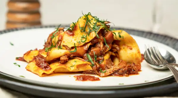 Herzhaftes Pasta Ragu mit breiten Nudeln, übergossen mit einer reichhaltigen Fleischsauce und garniert mit frischen Kräutern.