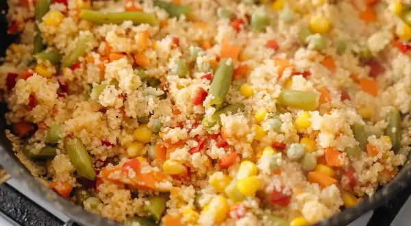 En varm och färgglad couscousrätt med gröna bönor, majs, morötter och paprika i en stekpanna.