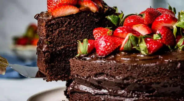 Ein hoher Schokokuchen mit frischen Erdbeeren und Schokoladenglasur wird angeschnitten.
