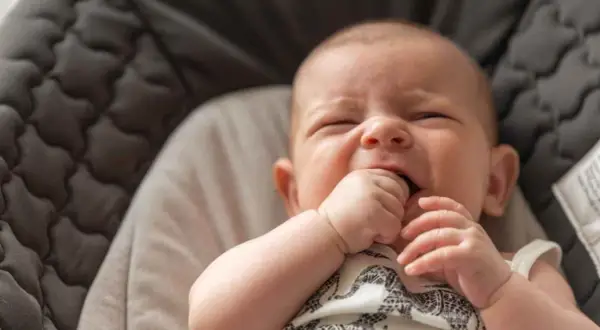 Un bebé de 3 meses no duerme, con los ojos cerrados y la mano en la boca, en una hamaca acolchada.