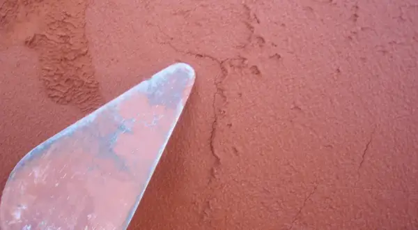 Una espátula rosa aplica mortero rojizo a una pared texturizada.