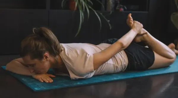 Femme pratiquant des exercices de yoga pour soulager la cruralgie, en position de cobra inversé sur un tapis bleu.