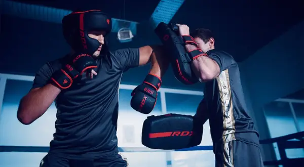 Two boxers in a ring, one wearing a headguard and gloves, practicing sparring with pads.