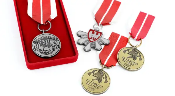 Odznaczenia strażackie w pudełku i luźno leżące na białym tle. Widać godło Polski i symbole strażackie.