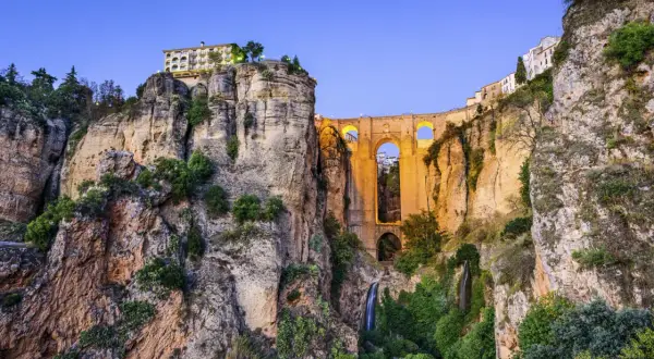 El Puente Nuevo de la Ronda, Málaga, se alza majestuoso sobre un profundo tajo, con cascadas y vegetación adornando sus acantilados.