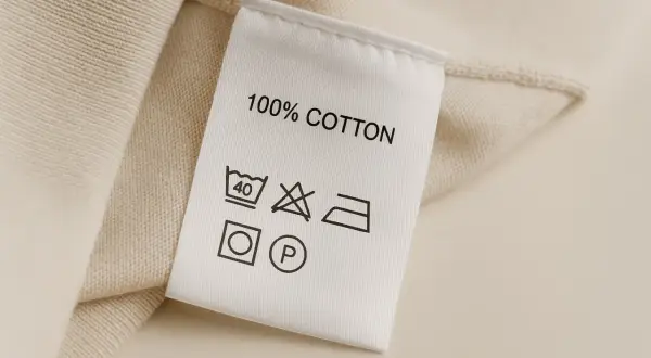 Metka z 100% bawełny. Zawiera skróty tkanin i symbole pielęgnacji: pranie w 40°C, zakaz wybielania, prasowanie, suszenie w suszarce i czyszczenie chemiczne.