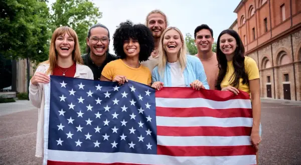 Grupo de jóvenes sonriendo y sosteniendo la bandera de EE.UU. ¡Un año de intercambio en Estados Unidos lleno de alegría!