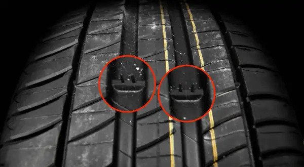 Gros plan sur un pneu de voiture, avec deux cercles rouges mettant en évidence les indicateurs d'usure. C'est un bon indice pour savoir quand changer ses pneus.