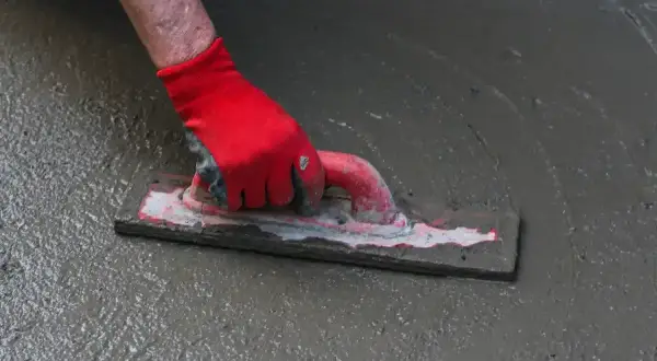 Dłoń w czerwonej rękawicy wygładza świeży beton kielnią. To kluczowy etap prac, gdzie dba się o równomierne rozłożenie materiału, co jest ważne dla późniejszego zbrojenia rozproszonego.