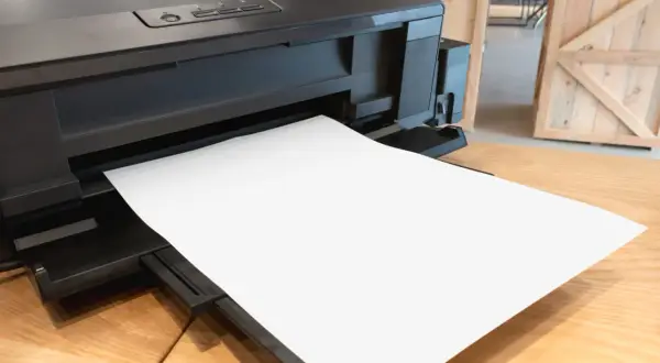 Czarna drukarka z pustą kartką papieru wysuniętą z podajnika.