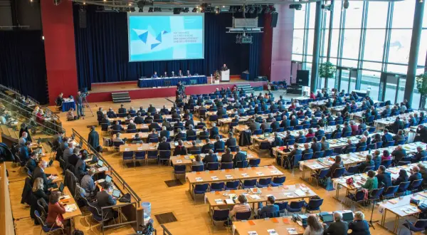 Große Versammlung mit vielen Zuhörern, die auf eine Bühne blicken. Die Bedeutung einer Synode wird hier durch die Präsentation und die Anwesenheit vieler Menschen verdeutlicht.