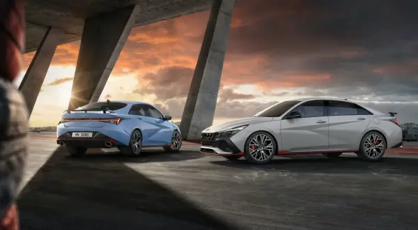Dwa sportowe Hyundai sedan w kolorach niebieskim i jasnoszarym stoją pod betonowym mostem podczas zachodu słońca.