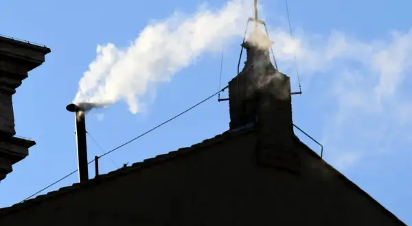 Biały dym z komina, jak sygnał wyboru nowego papieża, unosi się na tle błękitnego nieba.