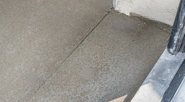 Szara betonowa posadzka z widoczną linią dylatacji biegnącą w kierunku narożnika budynku.