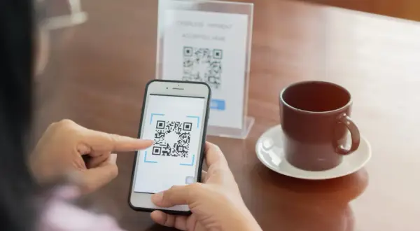 Osoba skanuje kod QR telefonem, by zapłacić bezgotówkowo. To prosty sposób, jak ściągnąć kod QR na telefon.