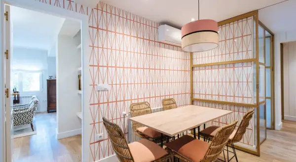 Comedor con papel pintado de rombos naranjas, mesa de madera y sillas de mimbre. Un ejemplo de como poner papel pintado para renovar tu hogar.