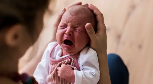 Ein Neugeborenes schreit laut, während es von Eltern gehalten wird. Die Frage, warum schreien Babys nach der Geburt, beschäftigt viele.