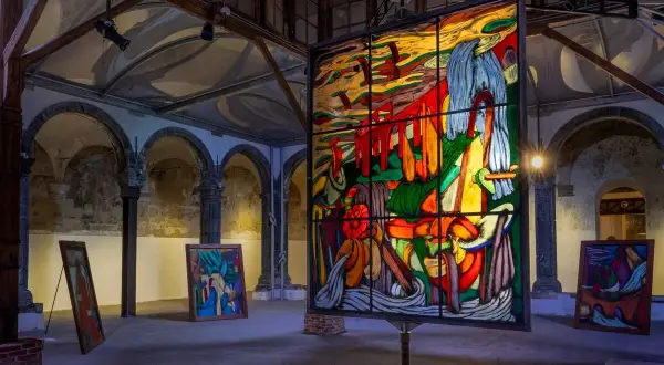 Vetrate colorate e quadri astratti in una galleria d'arte, con un'opera di ara starck al centro.