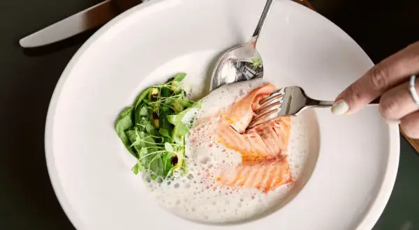 Ein zartes Lachsfilet mit Schaum und Grünzeug auf einem Teller. Ein Genuss in einem Berliner Fischrestaurant.