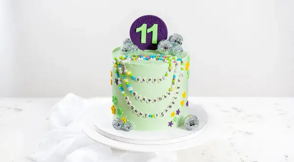 Eine bunte kinder torte für den 11. Geburtstag mit Perlenketten, Disco-Kugeln und Blumen.