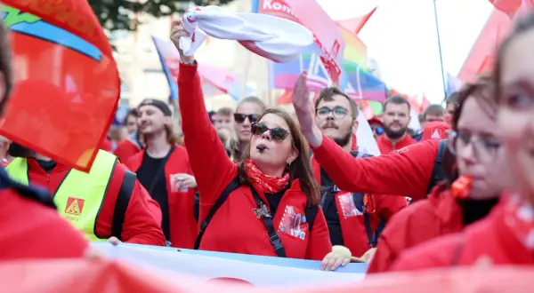 Frau mit Pfeife und weißem Tuch winkt, umgeben von roten Fahnen und Menschen bei einer Demonstration. Sie ist die Vorsitzende der IG Metall.