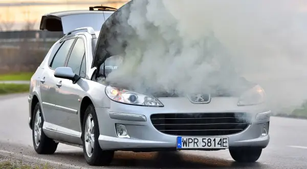 Srebrny Peugeot z otwartą maską i kłębami dymu. Chyba ten rozbiegany diesel potrzebuje pomocy.