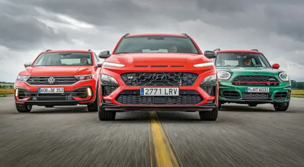 Trzy sportowe małe SUV-y: czerwony Volkswagen, pomarańczowy Hyundai i zielony Mini, jadące po drodze.