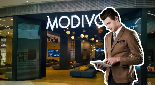 Elegancki mężczyzna w garniturze przegląda tablet przed sklepem MODIVO. W tle widać promocje CCC GPW.