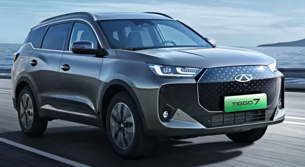 Szary SUV Chery Tiggo 7 z zielonym napisem TIGGO 7 na grillu, jadący po drodze.