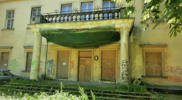 Zaniedbany pałac Tarnowskich w Krakowie, z zabitymi deskami oknami i drzwiami, pokryty graffiti.