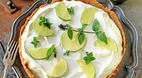 En krämig key lime pie med limeklyftor och mynta på en krispig botten.