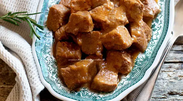 Un saporito spezzatino di vitello, la ricetta della nonna che profuma di casa. Servito su un piatto decorato con un rametto di rosmarino.