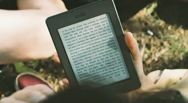 Une personne lit un livre sur une liseuse, profitant du soleil. L'encre numérique offre une lecture confortable en extérieur.